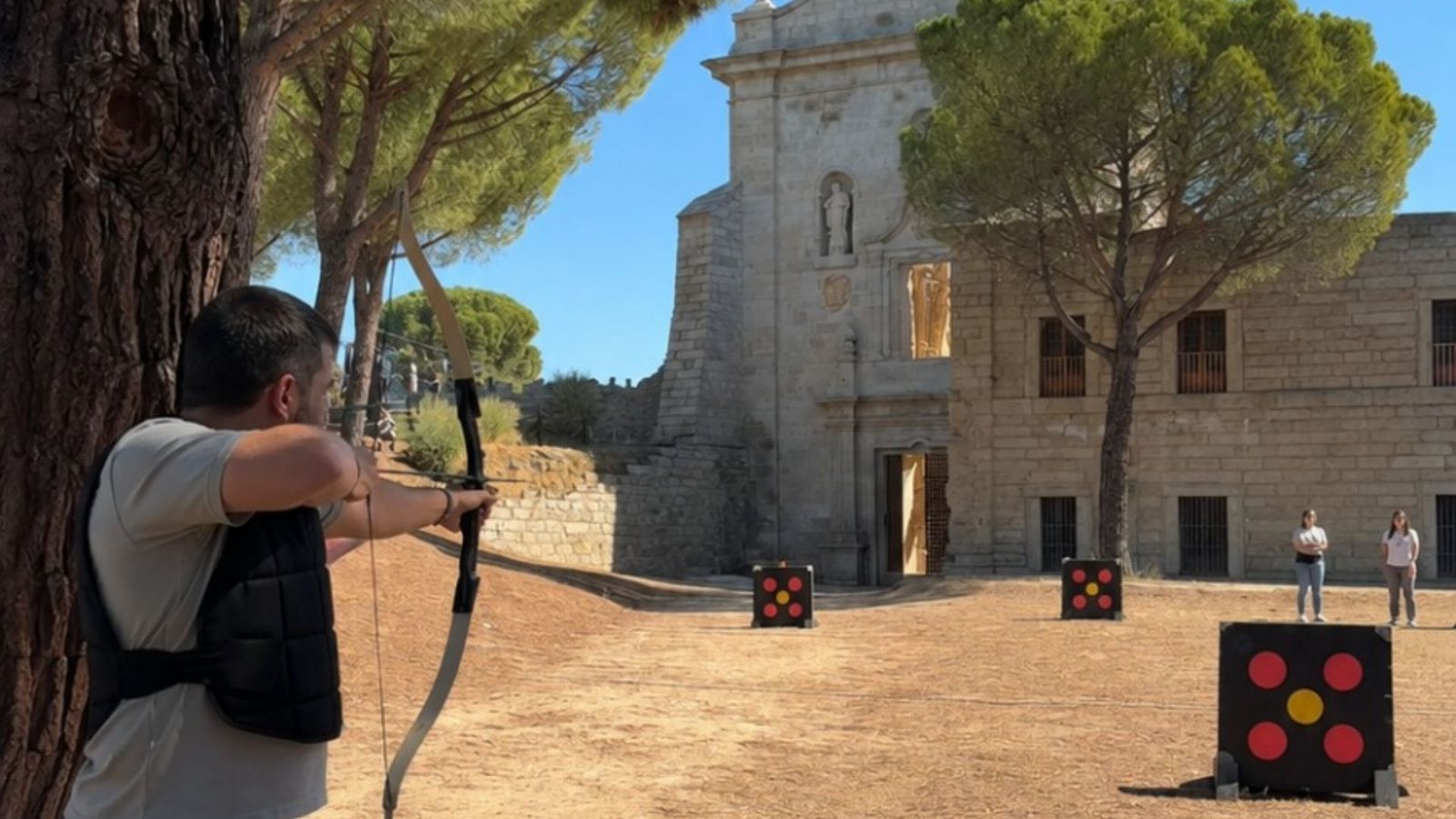 Participante tirando con arco frente a la fachada de piedra del monasterio